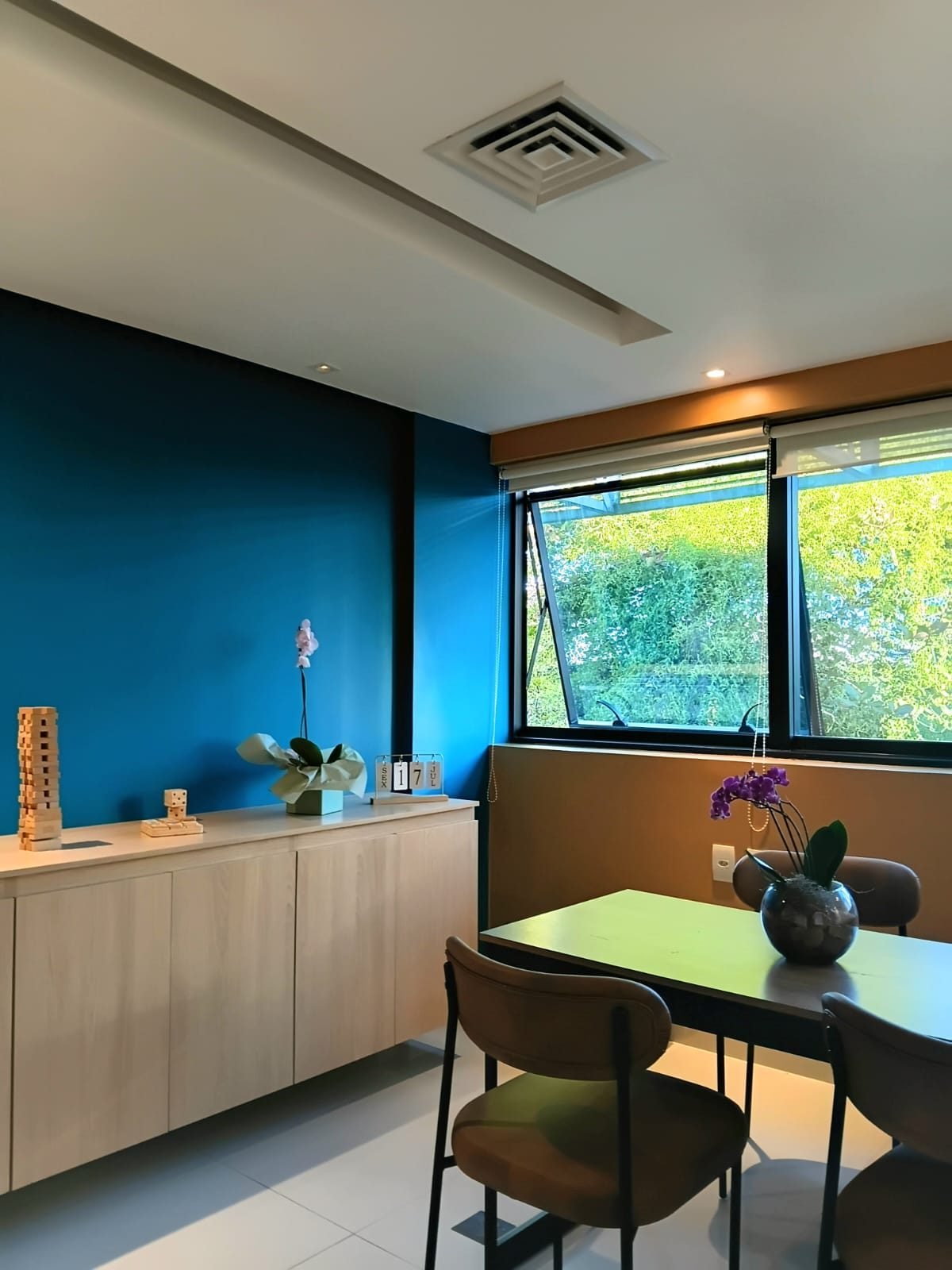 Sala de atendimento com mesa, cadeiras, armário claro e janela ampla com vista para árvores.